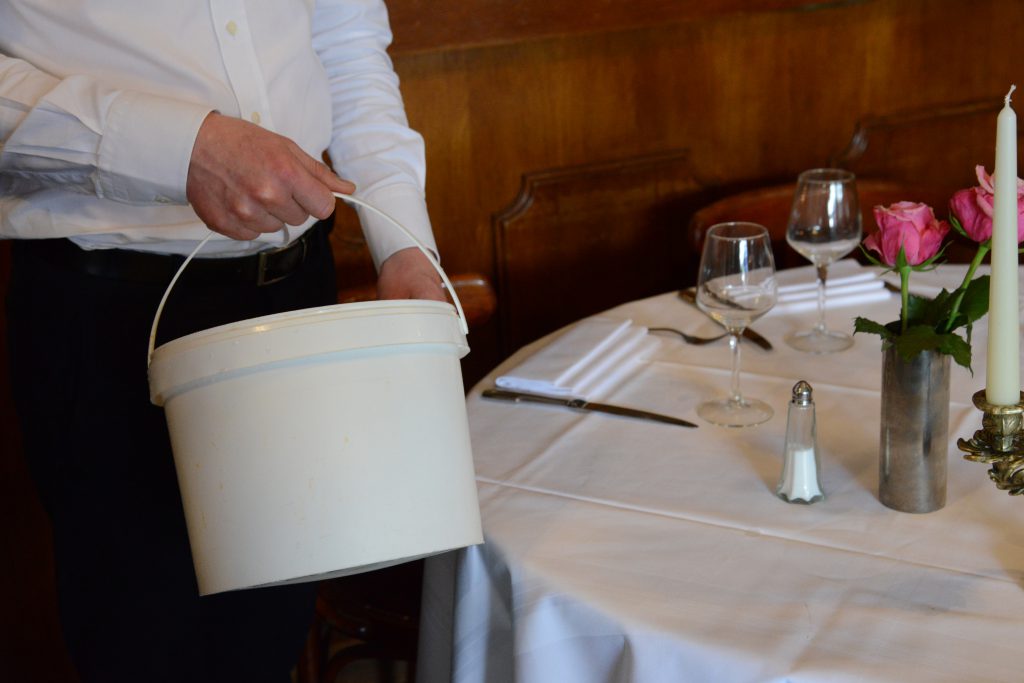 Waiter with bucket for restaurant leftovers, as different cultures have different solutions for the doggy bag. (Image © Meredith Mullins.)
