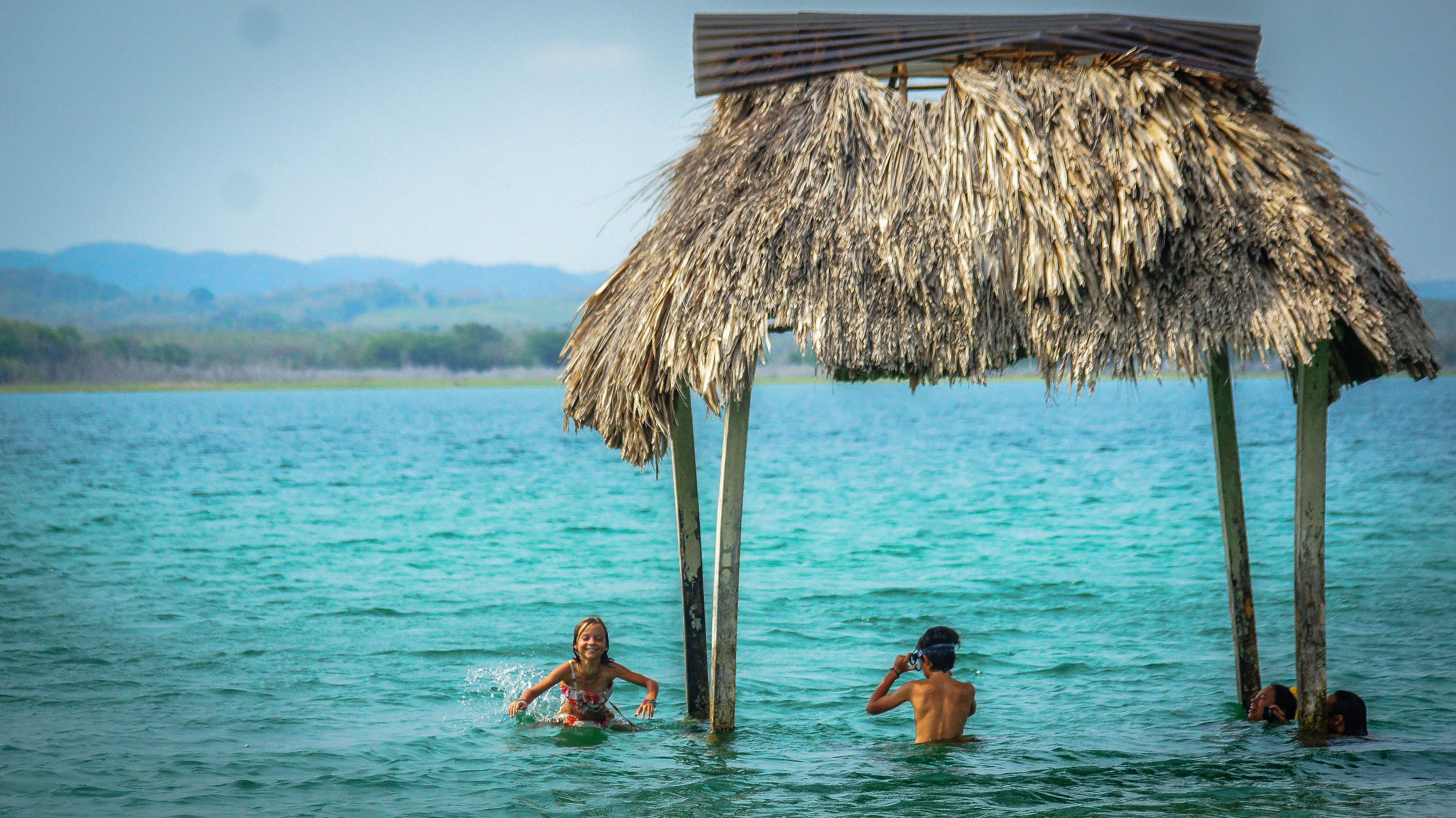 A young girl and boy playing in the water underneath a palapa in Guatemala, members of a traveling family that shares its wanderlust. (image © Sam Anaya A.).