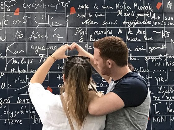 Couple in front of the Paris Wall of Love, seeing the many ways to say I Love You. (Image © Meredith Mullins.)