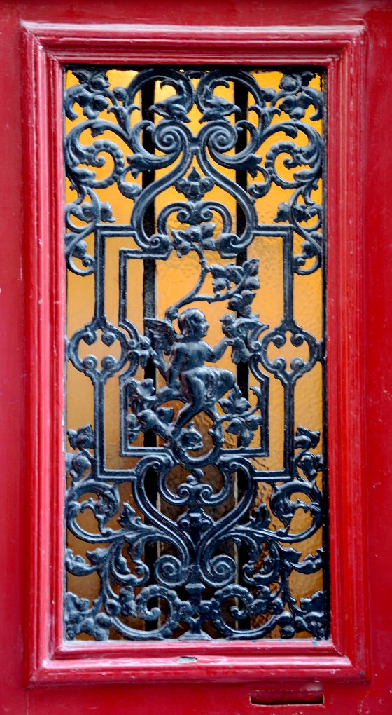 Red door with grill work of an angel and a dove in Paris, one of the Paris angels that serves as a cultural symbol. (Image © Rosemary Flannery.)