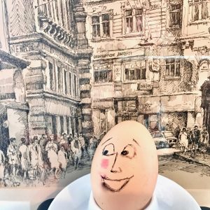 An egg character set against a scene of urban crowds becomes a metaphor for the fragility one can feel when speaking two languages. (Image © Joyce McGreevy)