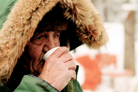Man in furry hood drinks coffee after receiving a random act of kindness of suspended coffee.