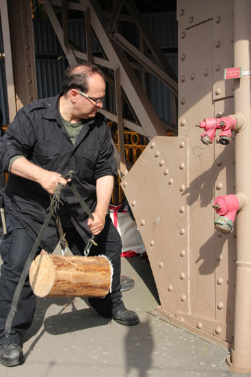 Joe Bertolozzi swinging a log into the Eiffel Tower structure, artistic expression in natural sounds.