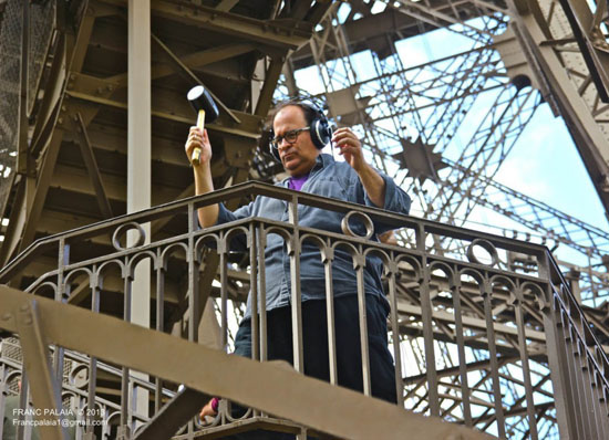 Joe Bertolozzi with rubber hammer on Eiffel Tower railing, a unique form of artistic expression.