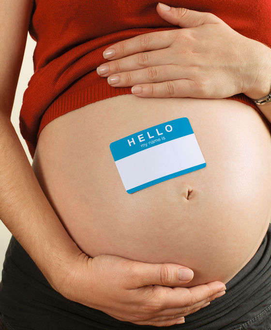 Pregnant woman with blank name tag on her stomach, illustrating the upcoming choice of a baby name that may follow a naming custom