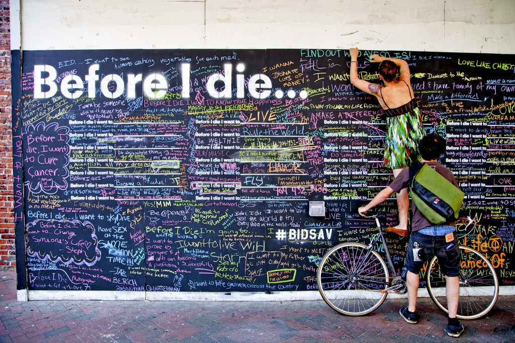 Girl writing on "Before I die" wall in Savannah, Georgia, where messages show that people are trying to gain perspective in their lives. Image © Trevor Coe.