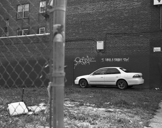 Car in vacant lot with graffiti on wall in Newark, NJ, artistic expression by Susan Berger on a photographic journey to capture images of America (© Susan Berger)   