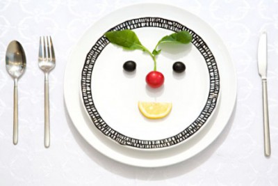 Dinner plate with face made from black olives for eyes, red radish for nose, its green leaves for eyebrows, and a lemon slice for a smile, showing the fun of creativity. (Image © Julia Saponova / Hemera)