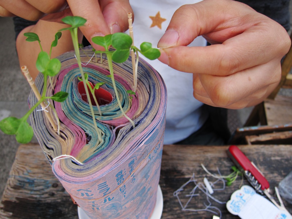 Tying up radish seedlings that sprout from the pages of Japanese manga comics, symbolizing the need to take care of good ideas in the creative process. (Image © Koshi Kawachi)