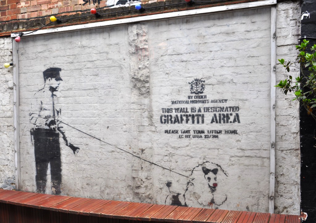 Creative street art by a British street artist known as Banksy, showing a policeman walking a highly groomed poodle in front of a satirical sign that declares the area as one designated for graffiti and requires passersby to take their litter home. (Photo © Sheron Long.