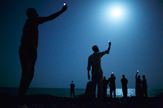 African migrants hold their phones to catch a signal, life lessons in connection and migration via photojournalism (Photo © John Stanmeyer)