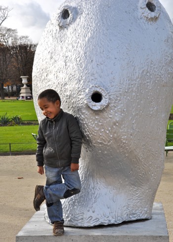 Boy climbing on a modern art sculpture of a large head in the Tuileries Gardens. (Image © Robert Long)
