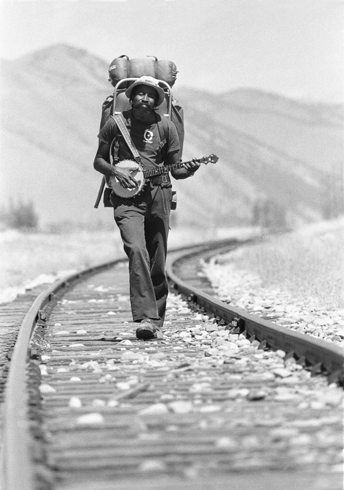 John Francis playing a banjo and walking down a railroad track, illustrating a traveler's long-distance walk across America. (Image © Glenn Oakley)