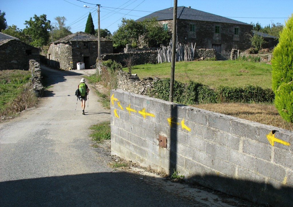 Pilgrim walking down a road through a town, showing travel inspiration of walking the Camino de Santiago. (image © Jenna Tummonds 