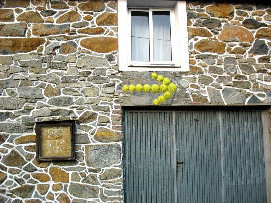 Yellow arrow made out of scallop shells mortared into the rock wall of a house along the Camino de Santiago, a route walked by many pilgrims with different travel inspiration. (Image © Jenna Tummonds)