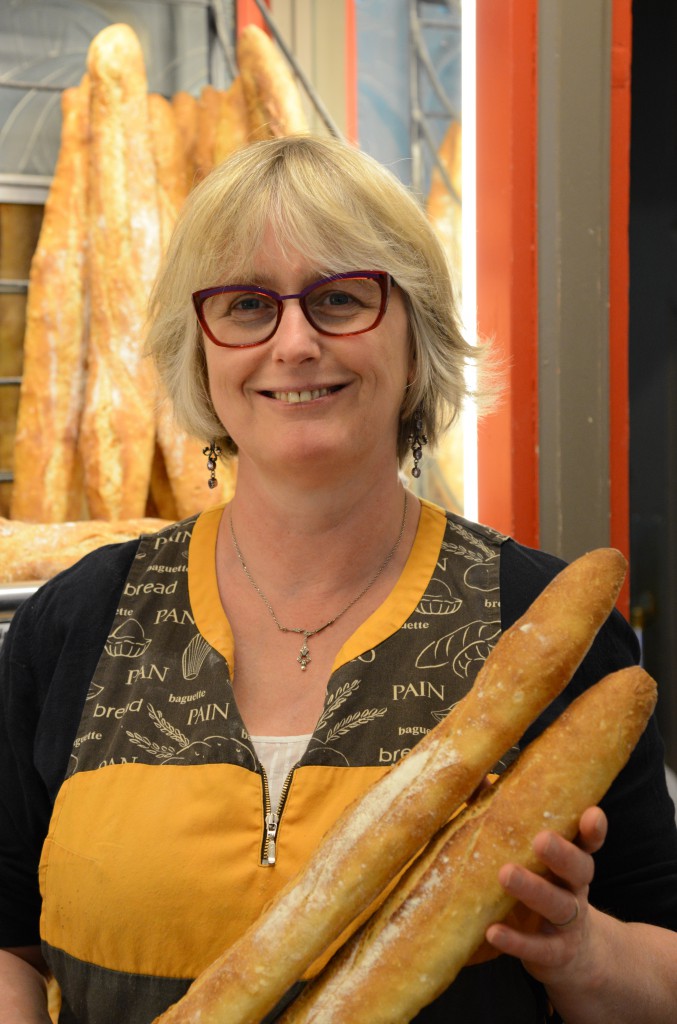 Woman in boulangerie with baguettes, Madame Martin, showing the focus on food of French sayings. (Image © Meredith Mullins)