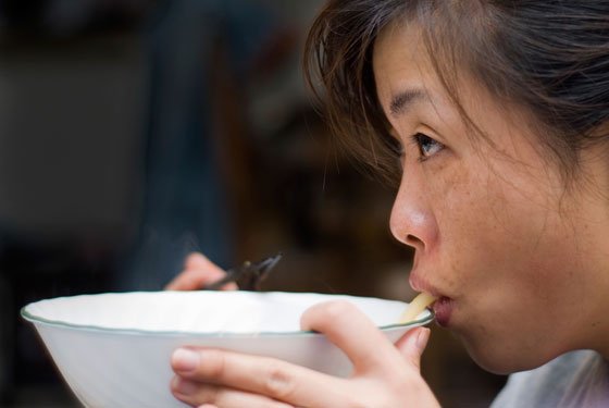 A woman slurping a noodle from a soup bowl, demonstrating different cultural do's and taboos at lunch around the world. (Image © Sean Barley / iStock)