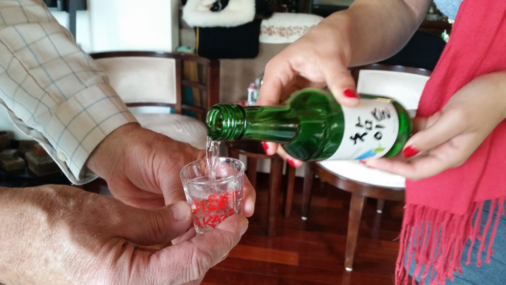 A young lady using both hands to pour soju for her father at lunch, illustrating respect for cultural do's and taboos. (Image © Sally Baho)