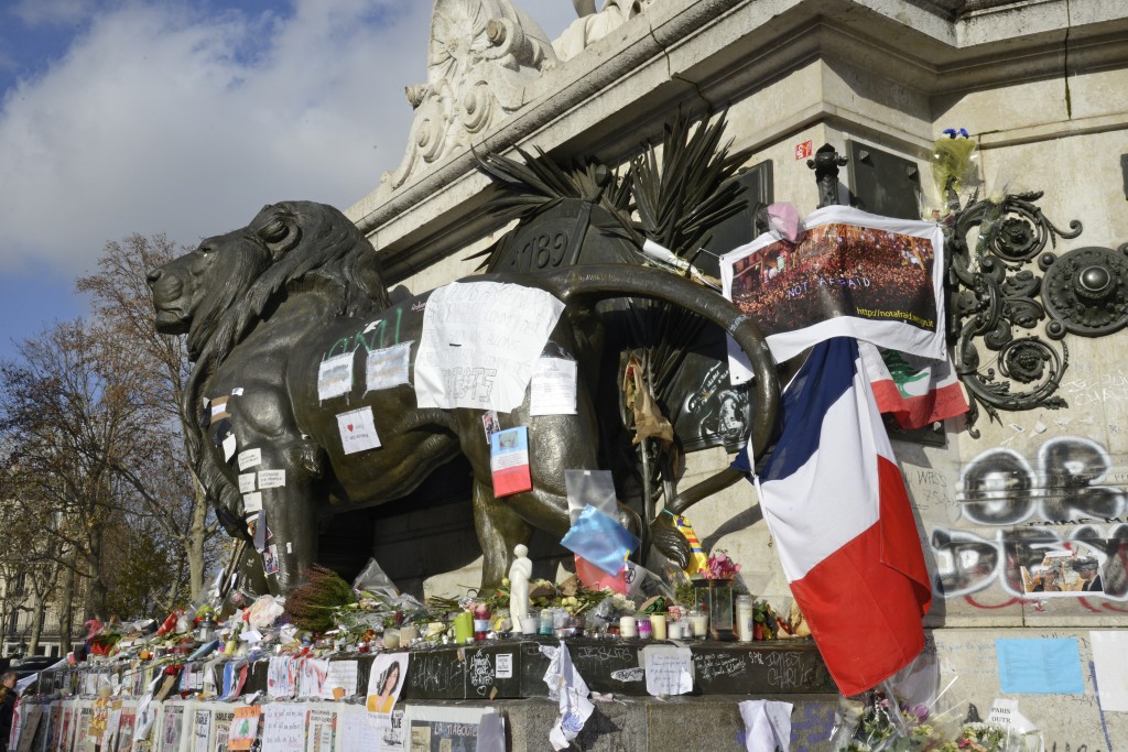 Flags and flowers for the Paris attacks at the Lion in the Place de la République in Paris, showing the cultural beliefs of the French. (Image © Meredith Mullins.)