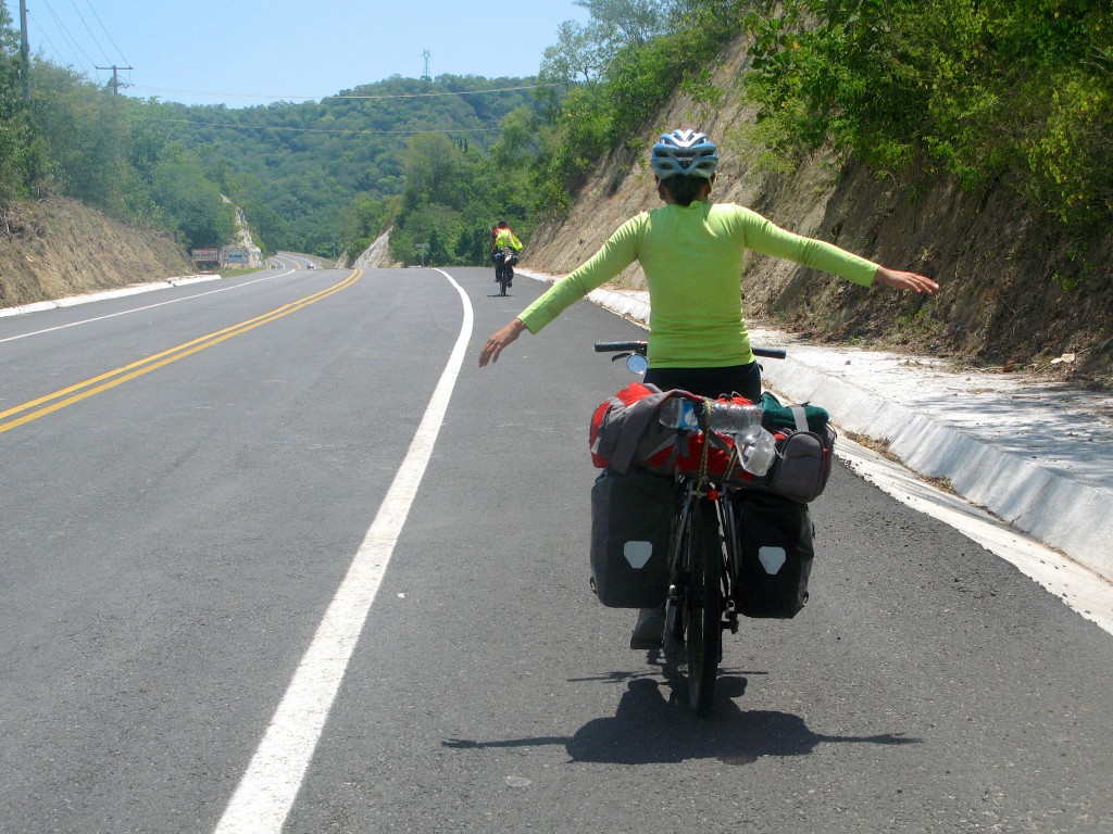 Biker riding with hands in the air, demonstrating the appreciation of living only with the survival essentials during adventure cycling along Mexican toll roads. (Image © Eva Boynton)