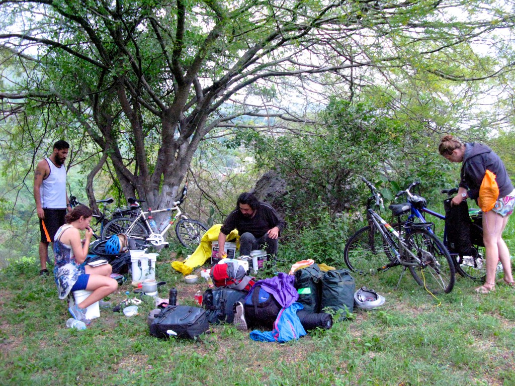 People setting up camp under a tree during adventure cycling along Mexican toll roads, showing how a place to camp is a survival essential. (Image © Eva Boynton).