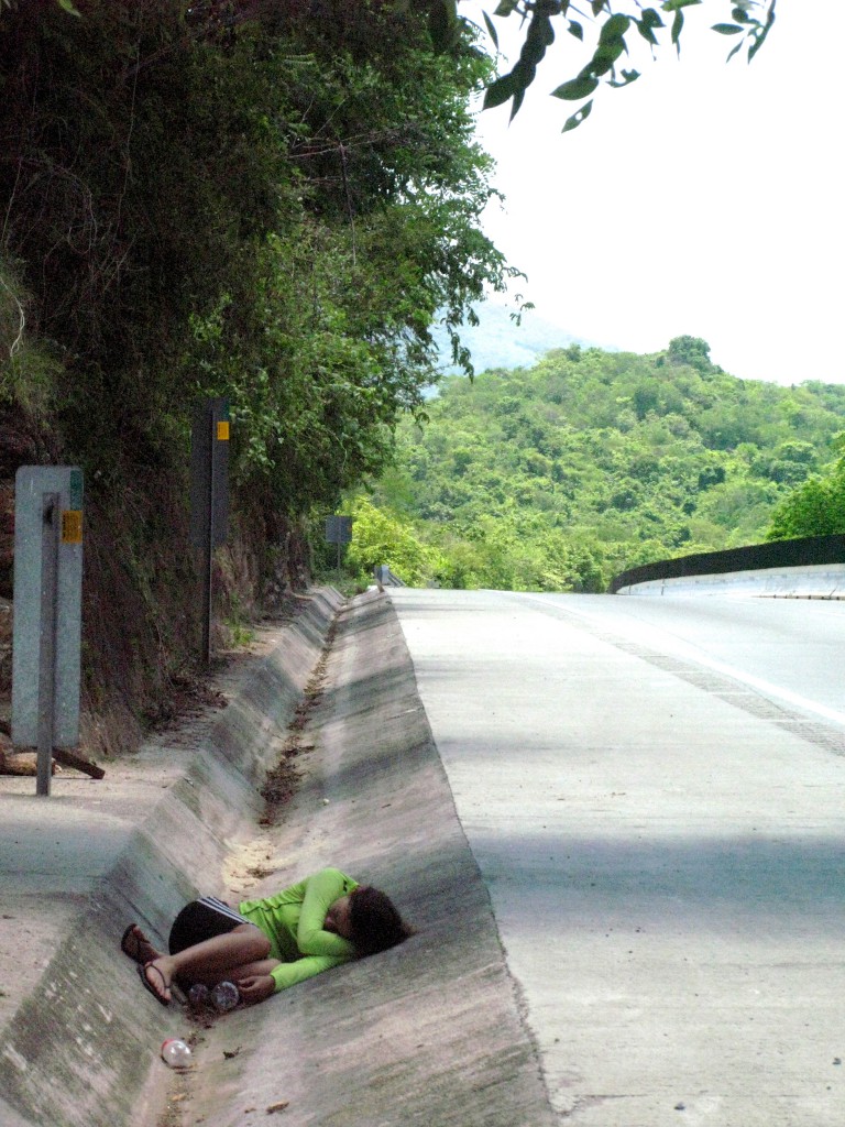 A girl sleeping on the side of the road during adventure cycling along Mexican toll roads, showing how shade is a survival essential. (Image © Eva Boynton).