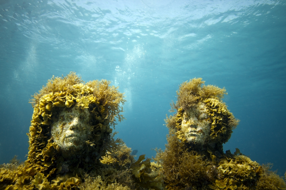Two sculptures covered in plant growth in the underwater museum of Jason deCaires Taylor, showing innovation by both artist and ocean. (Image © Jason deCaires Taylor)