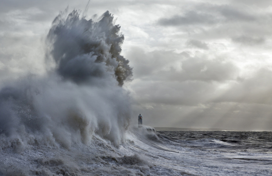 Waves threatening Porthcawl lighthouse, with light rays in the background, one of the most amazing places on earth to photograph. (Image © Steven Garrington.)