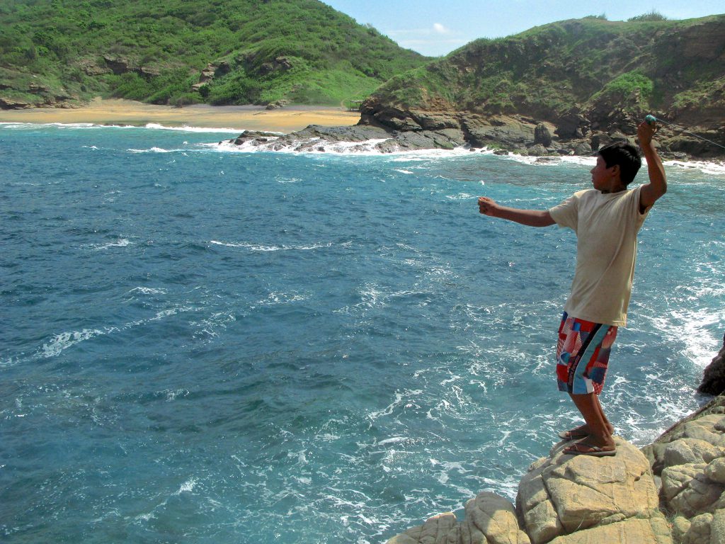 A boy throwing a fishing line into the ocean, as he demonstrates part of fishing lessons learned during an authentic cultural experience in Mexico. (image © Eva Boynton)