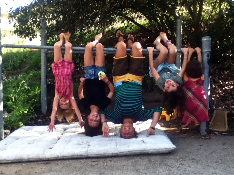 Kids and WWOOFer hanging upside down on a pole, showing the education in family dynamics for a global citizen (image © Eva Boynton).