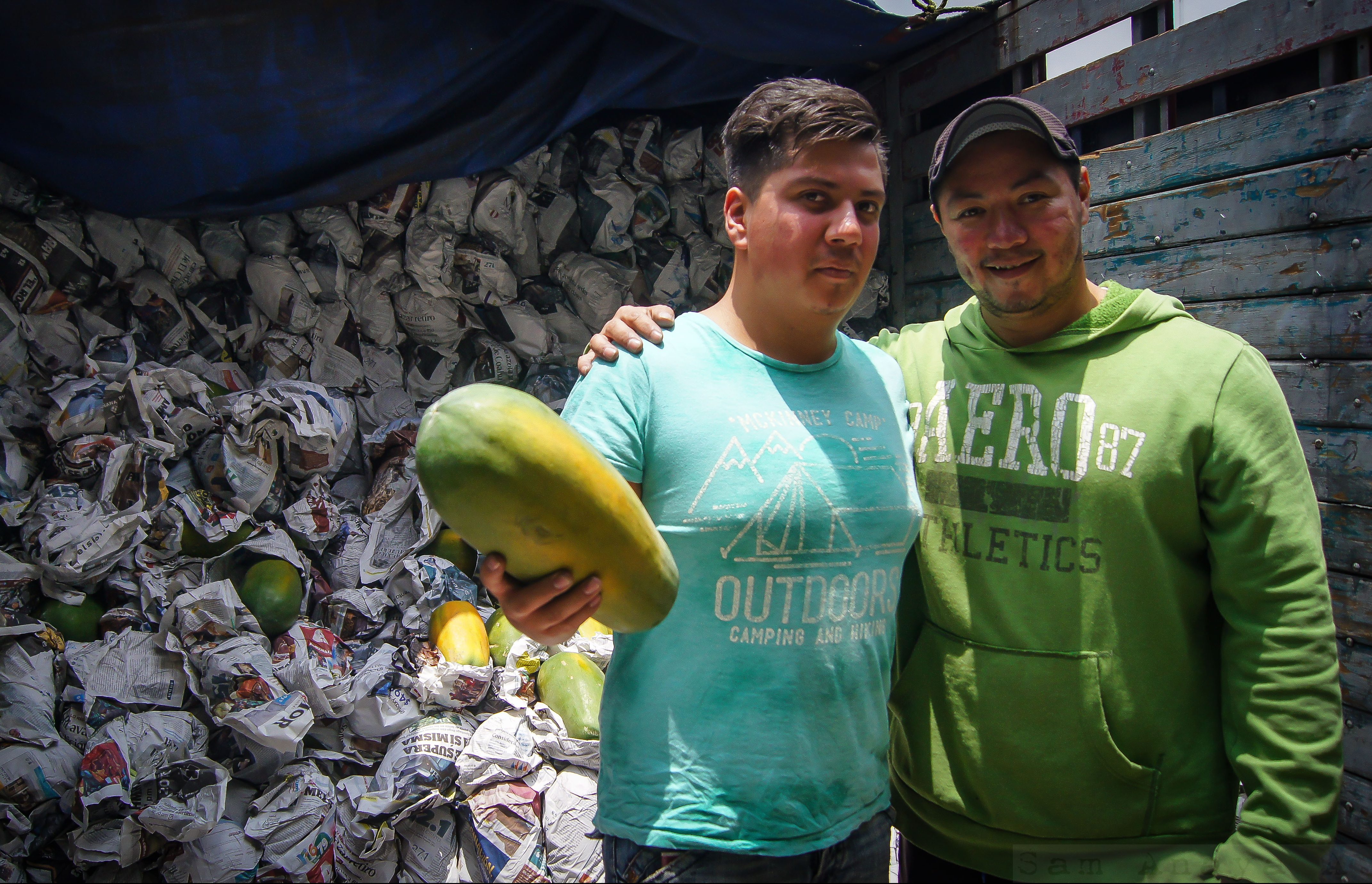 Two vendors holding a papaya in front a stack of papayas wrapped in newspapers at the Central de Abasto, the world's largest wholesale market where Mexico's cultural heritage is also on display. (image © Sam Anaya A.)