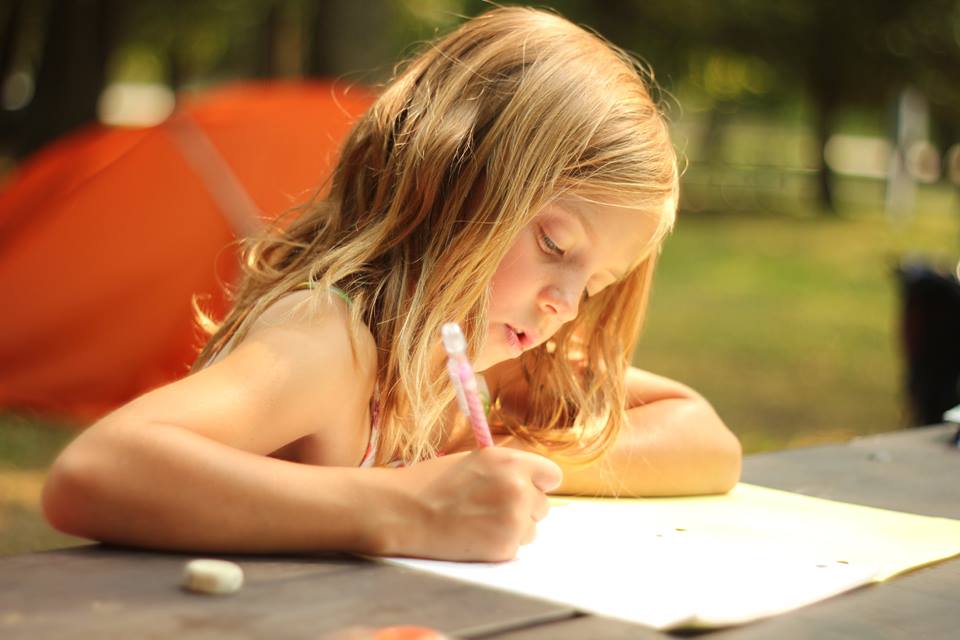 A young girl, part of a traveling family, draws at a picnic table, as she experiences her family's legacy of wanderlust. (image © Conk Family)