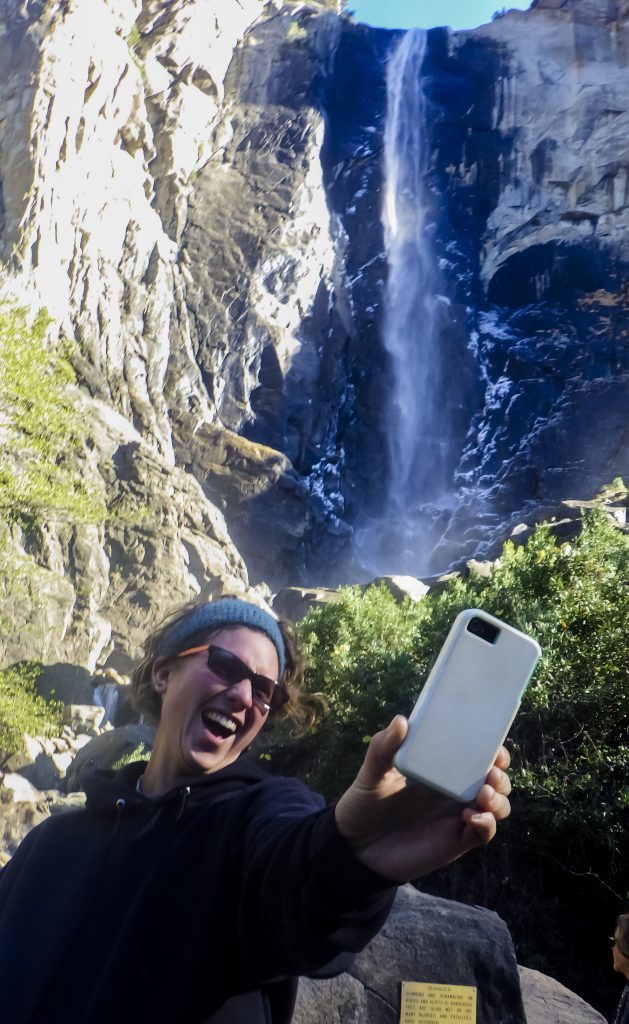 A woman takes a selfie at Yosemite Falls, illustrating how you can forget to open your eyes and experience Yosemite. (image © Eva Boynton)