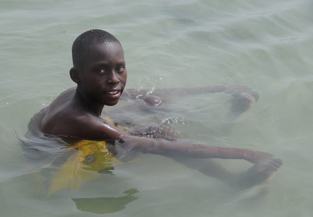 Senegal boy resting in the ocean in M'Bour, offering travel adventures and a photographer's dream in images. (Image © Meredith Mullins.)