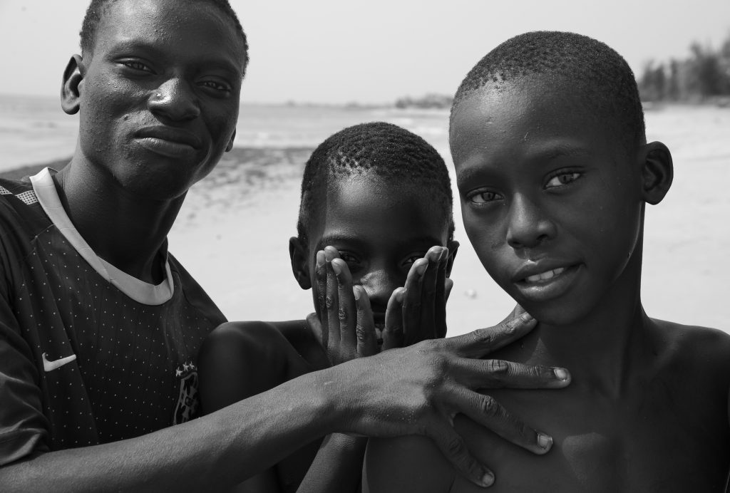 Three Senegalese boys (B&W) on the beach in M'Bour, Senegal, offering travel adventures and a photographer's dream in photos. (Image © Meredith Mullins.)