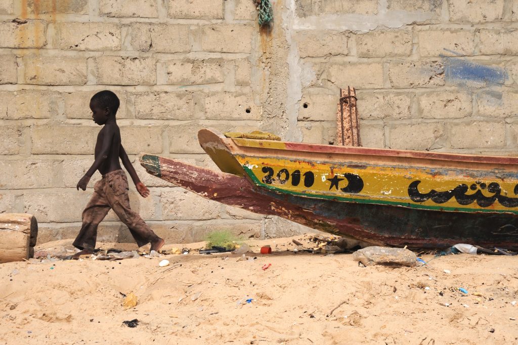 Boy and boat in M'Bour offering travel adventures and a photographer's dream with vivid Senegal life. (Image © Meredith Mullins.)