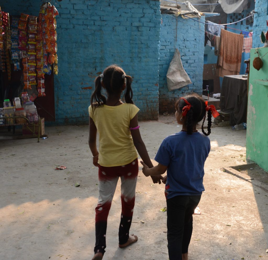 Two girls hold hands at the Kathputli Colony in Delhi, showing cultural encounters in the slums of India. (Image © Meredith Mullins.)