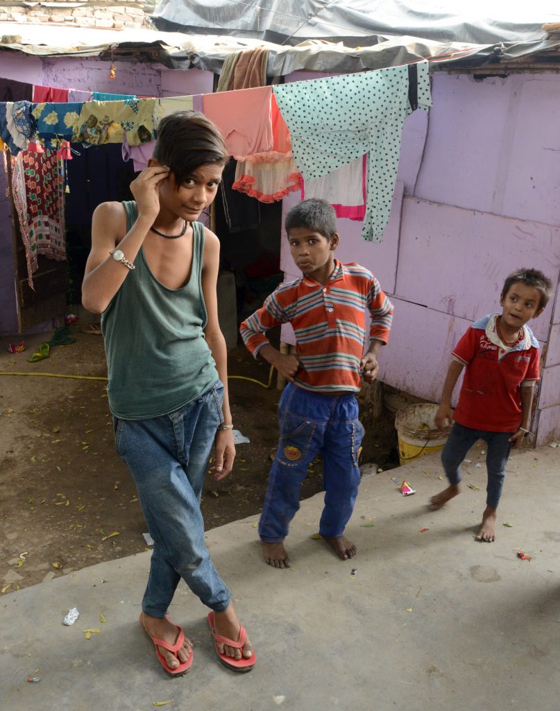 Three children of the Kathputli Colony in the street, showing cultural encounters in the slums of India. (Image © Meredith Mullins.)