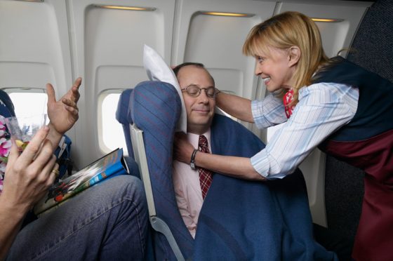 Flight attendant adjusting a pillow for excellent customer service, offering travel adventures and air travel stories worth remembering. (Image © Digital Vision.)