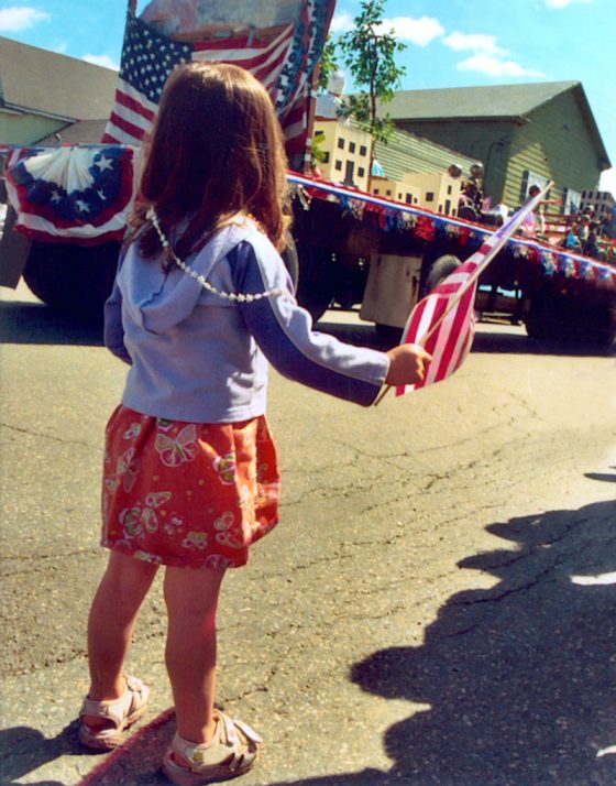 Young girl with American flag at parade, part of crossing cultures to celebration Independence Day. (Image © iStock/SaraPlacey.)