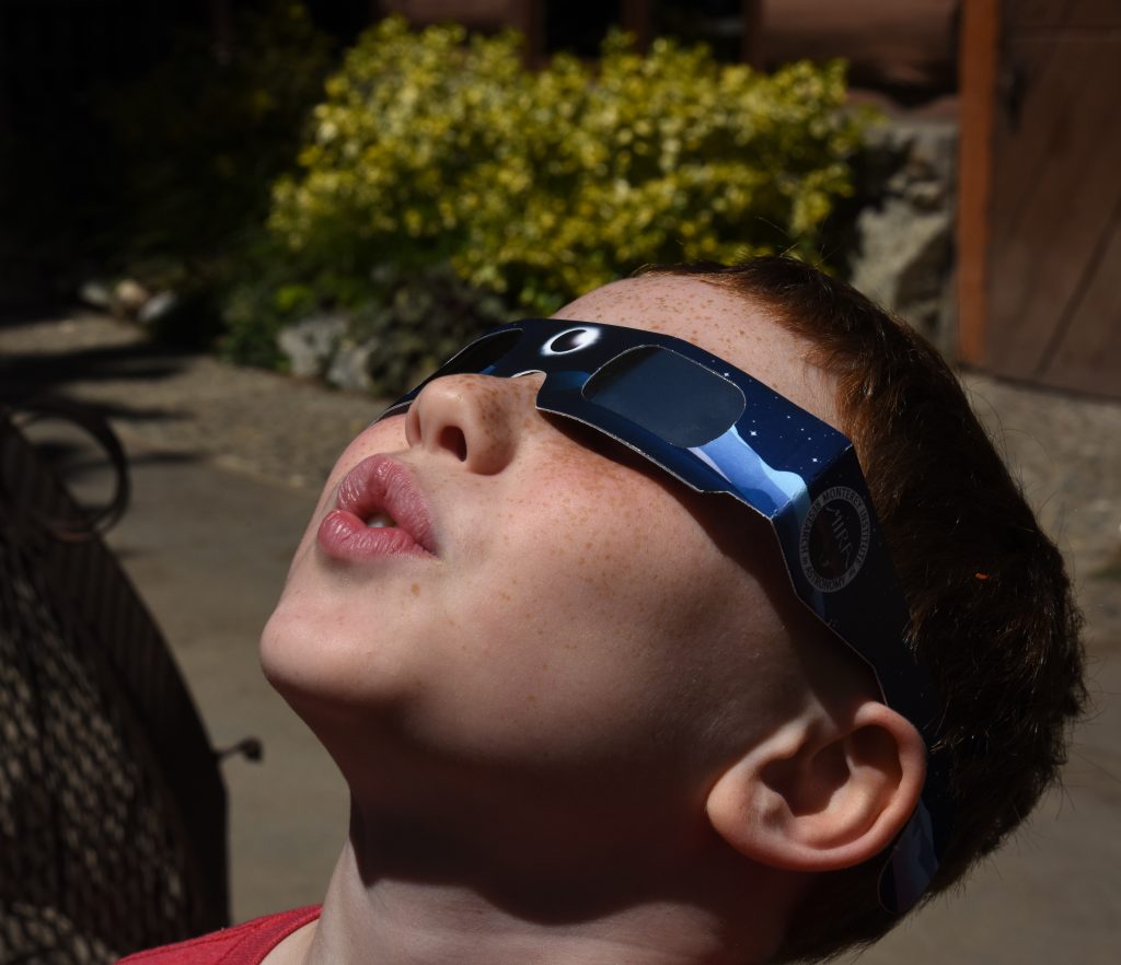 Boy looking up at sun with eclipse glasses, travel inspiration for the 2017 total solar eclipse. (Image © Meredith Mullins.)