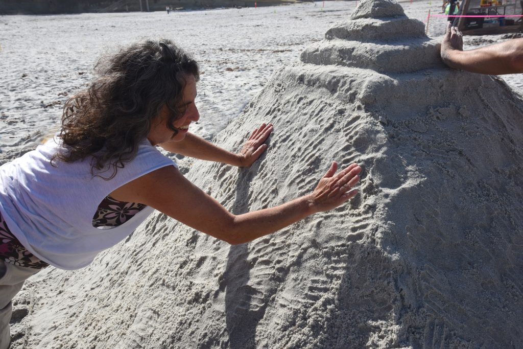 Woman patting sand sculpture by hand at the Great Carmel Sand Castle Contest, where entrants are discovering the art of sand sculptures. (Image © Meredith Mullins.)