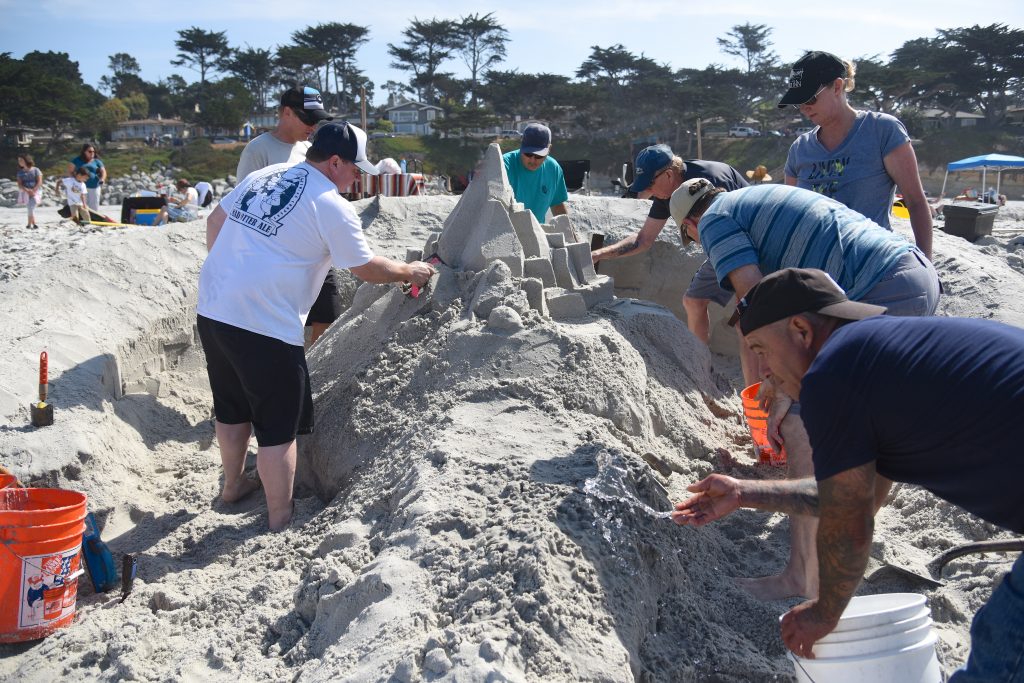 Team of sand sculptors work on a sand sculpture at the Great Carmel Sand Castle Contest, discovering the art of sand sculptures. (Image © Meredith Mullins.)