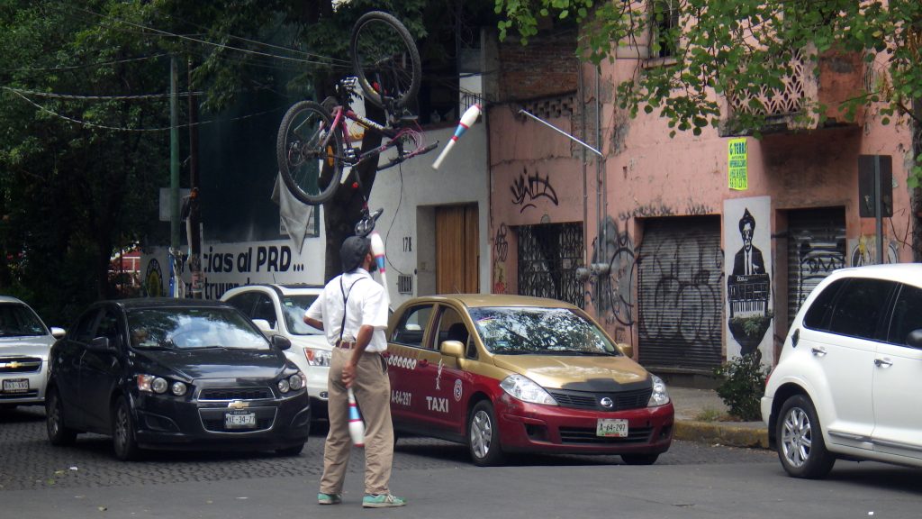A man juggles while balancing a bicycle on his head in Mexico City, showing life in Mexico City (image © Eva Boynton). 