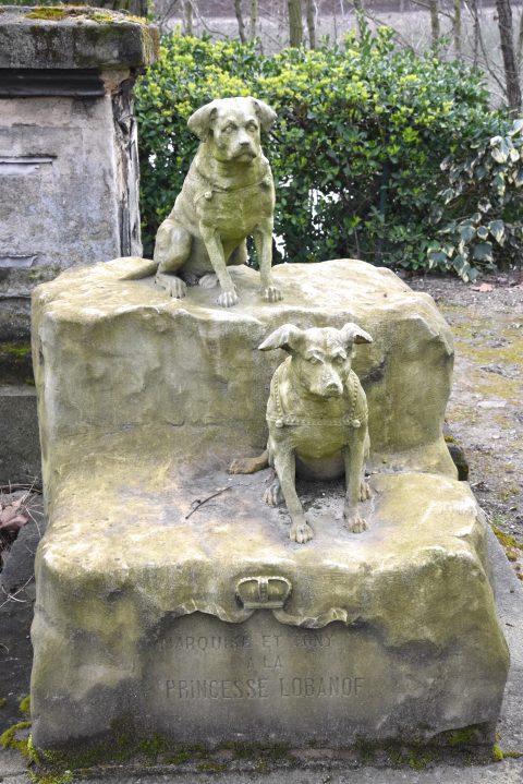 Two sculpted dogs on a grave in the Paris pet cemetery, showing cultural traditions of saying farewell to pets. (Image © Meredith Mullins.)