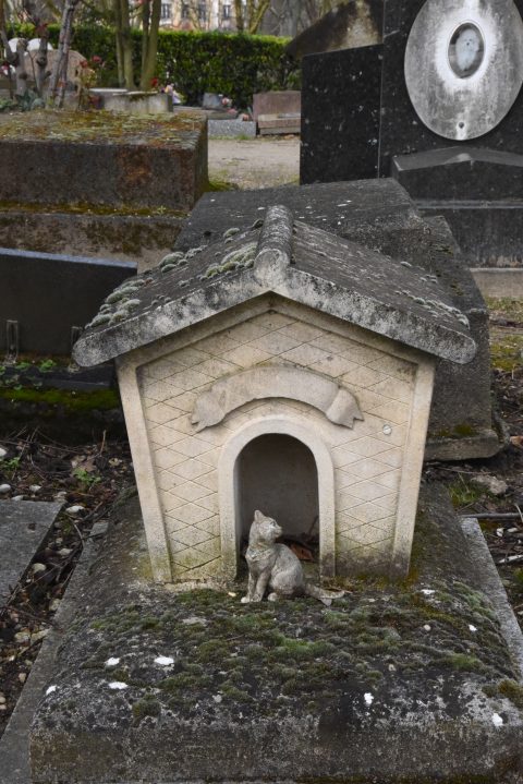 Doghouse tombstone with cat sculpture at the Paris pet cemetery, showing cultural traditions of saying farewell to pets. (Image © Meredith Mullins.)