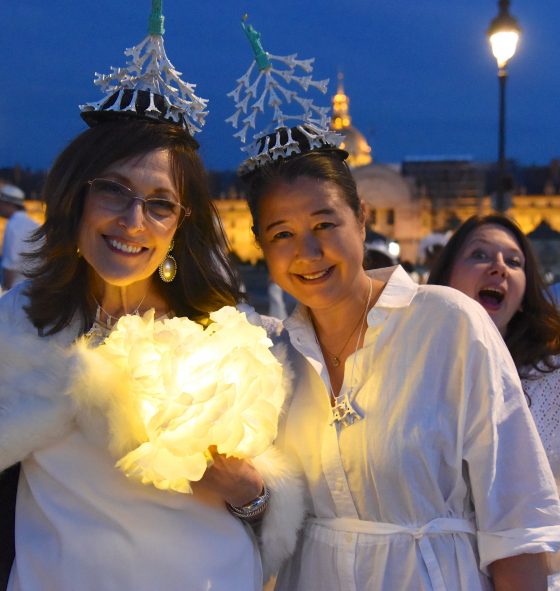 Women with Eiffel Tower headgear at the Paris Dîner en Blanc, enjoying the cultural traditions of the Dinner in White. (Image © Meredith Mullins.)