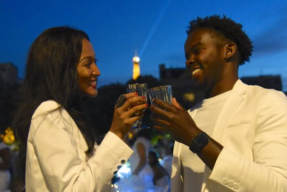 Two people toasting in front of the Eiffel Tower at the Paris Dîner en Blanc, enjoying the cultural traditions of the Dinner in White. (Image © Meredith Mullins.)