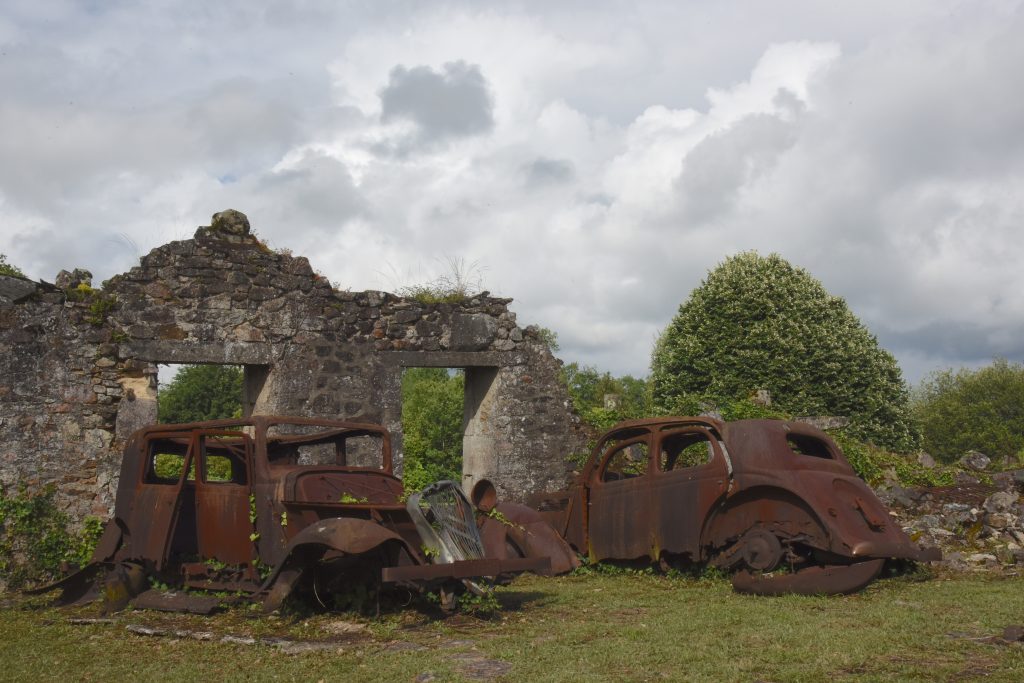 Rusted out cars in front of a burned out building in Oradour sur Glane, France, the site of the cultural history of a Nazi massacre during WW II. (Image © Meredith Mullins.)