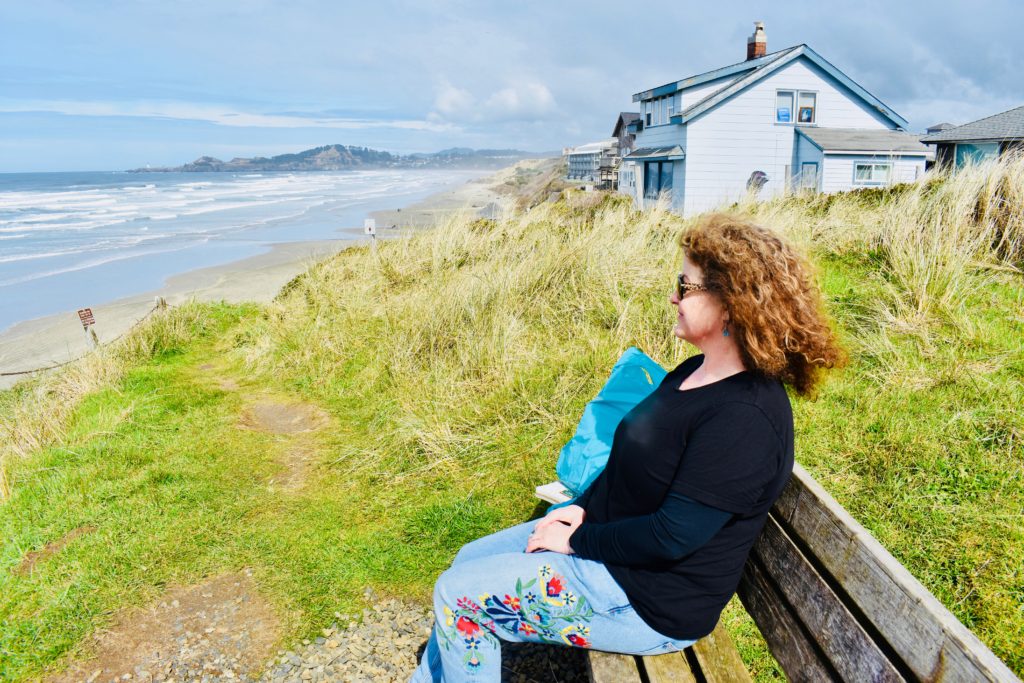 A woman sitting by the Oregon shore suggests why savoring summer can be a life-changing experience. (Image @ Joyce McGreevy)